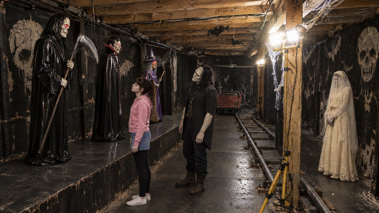 Gang einer Geisterbahn mit drei Animatronics auf einem Podest, davor eine junge Frau und das Monster, rechts an der Wand die Braut.